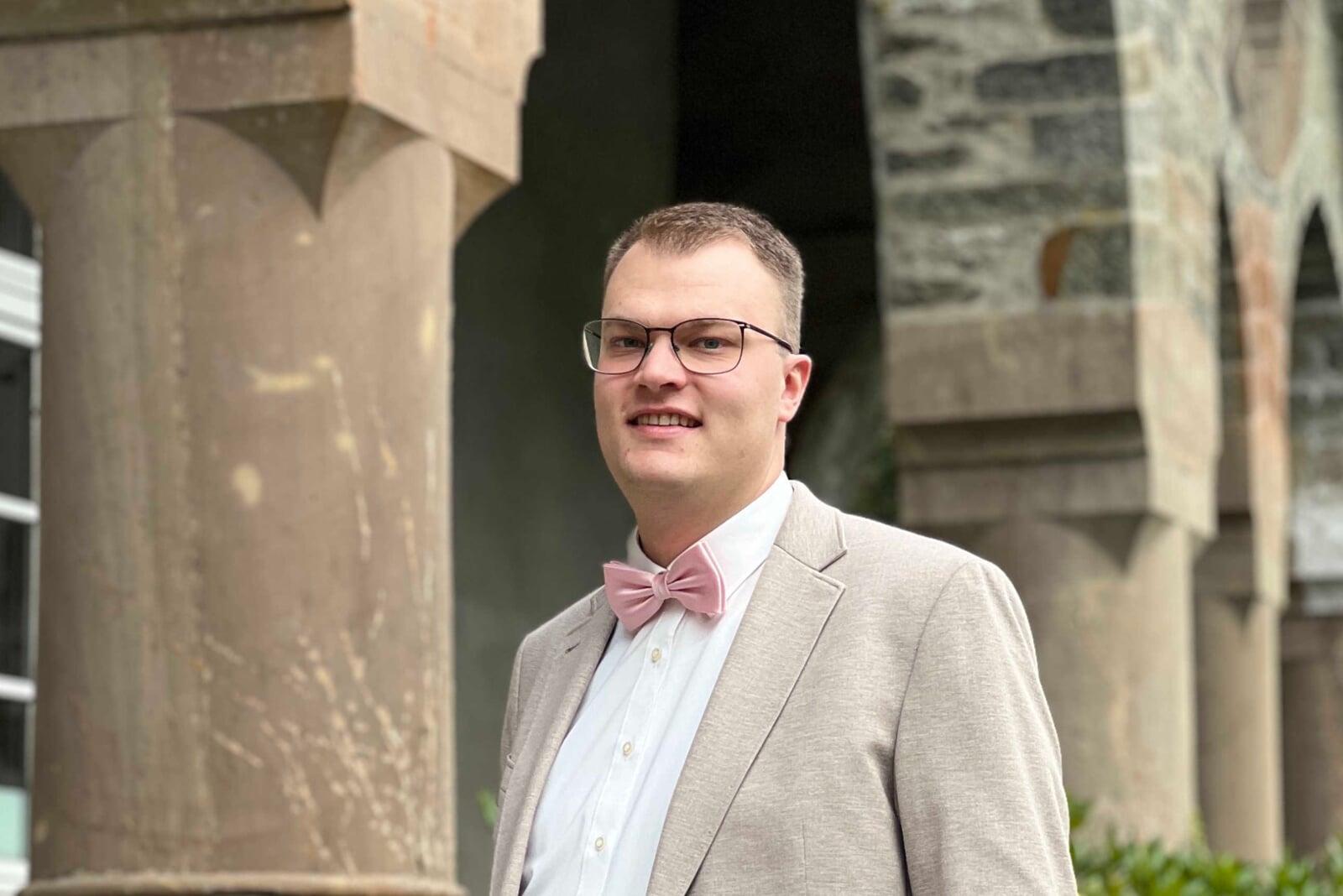 Matthias Bückert, Copywriter, im beigen Anzug mit Fliege vor einer Steinfassade